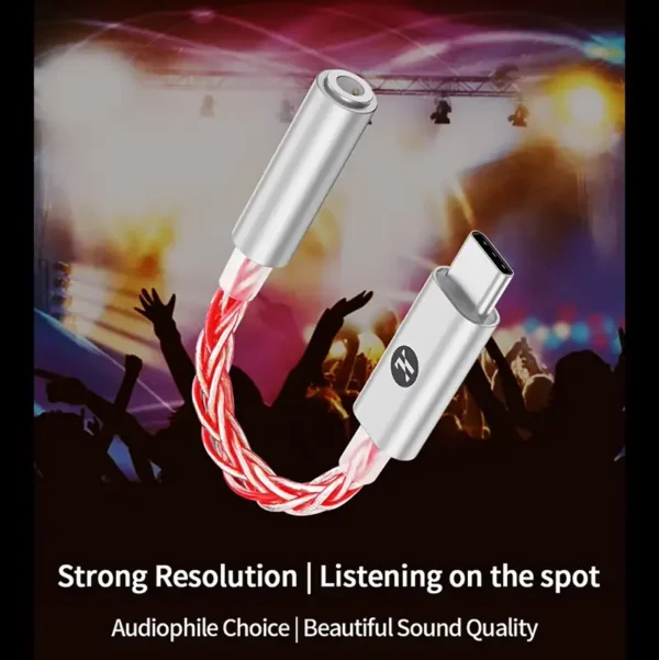 A close-up of a premium JCALLY JM6 Pro Type-C to 3.5mm audio adapter with its signature twisted red and silver-plated cable and metal connectors. The image includes text: "Strong Resolution | Listening on the spot" and "Audiophile Choice | Beautiful Sound Quality" against a blurred live music crowd background. This adapter is the perfect choice for high-quality audio on-the-go and competitive gaming.